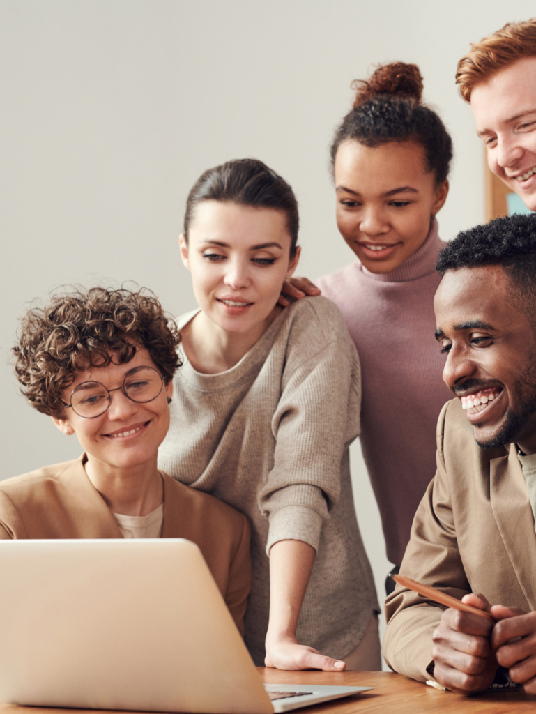 A diverse creative team collaborating on a digital project, looking at a laptop with positive expressions.